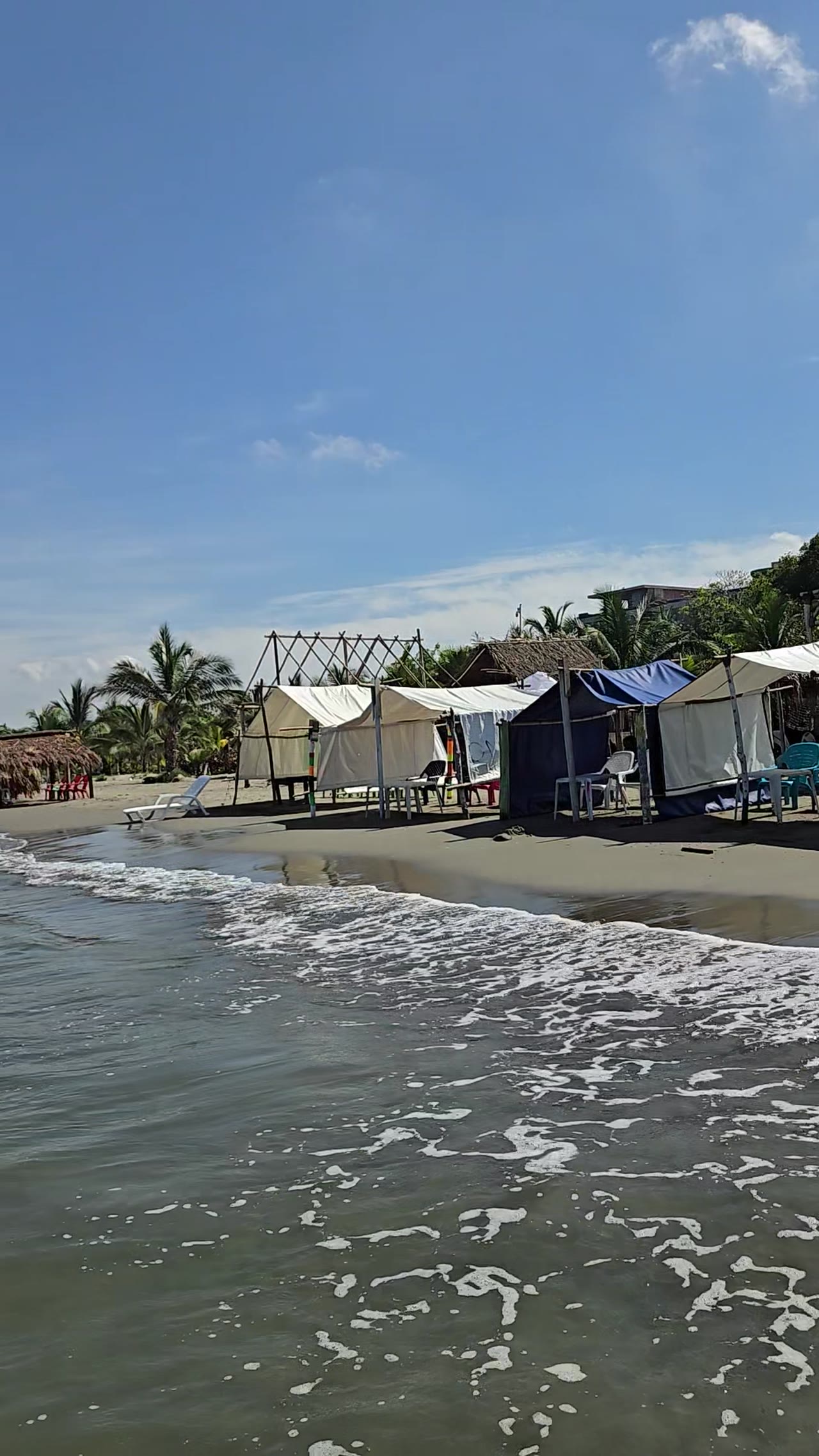 Canvas tents along the shore at Playa Muralla with waves and palm trees